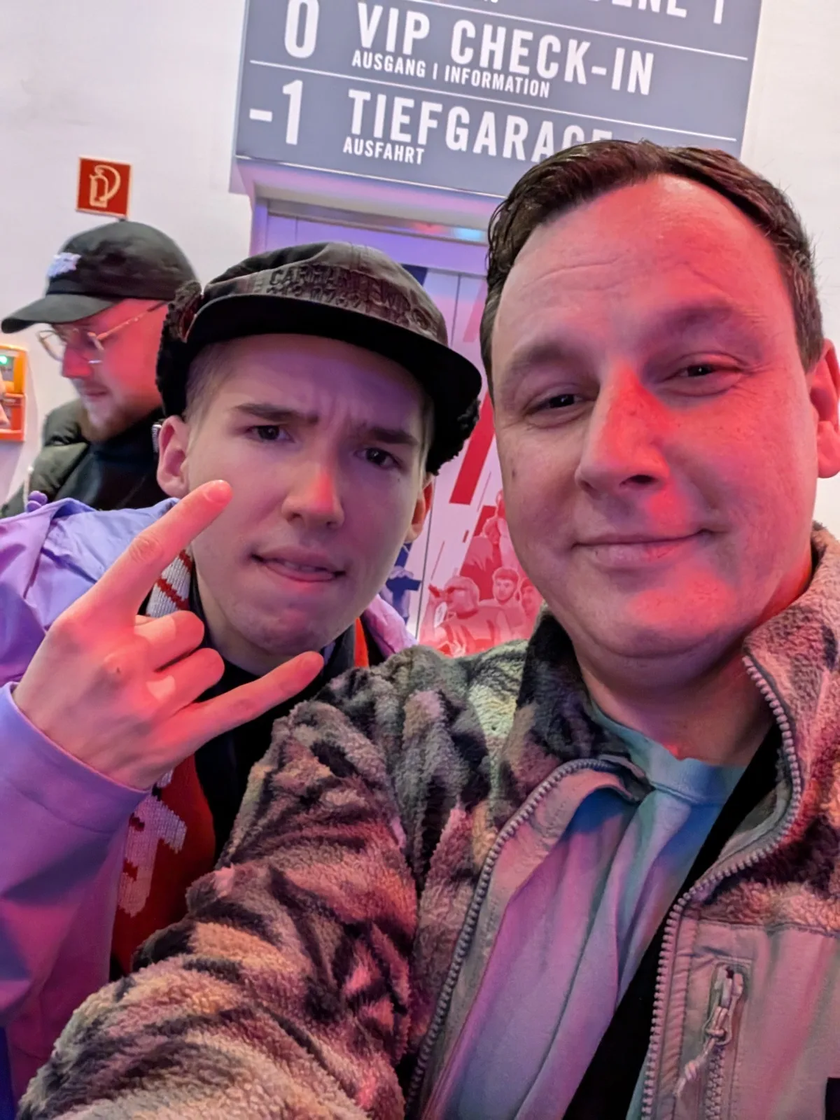 Selfie von zwei Männern unter den Hinweisschildern einer Veranstaltungshalle