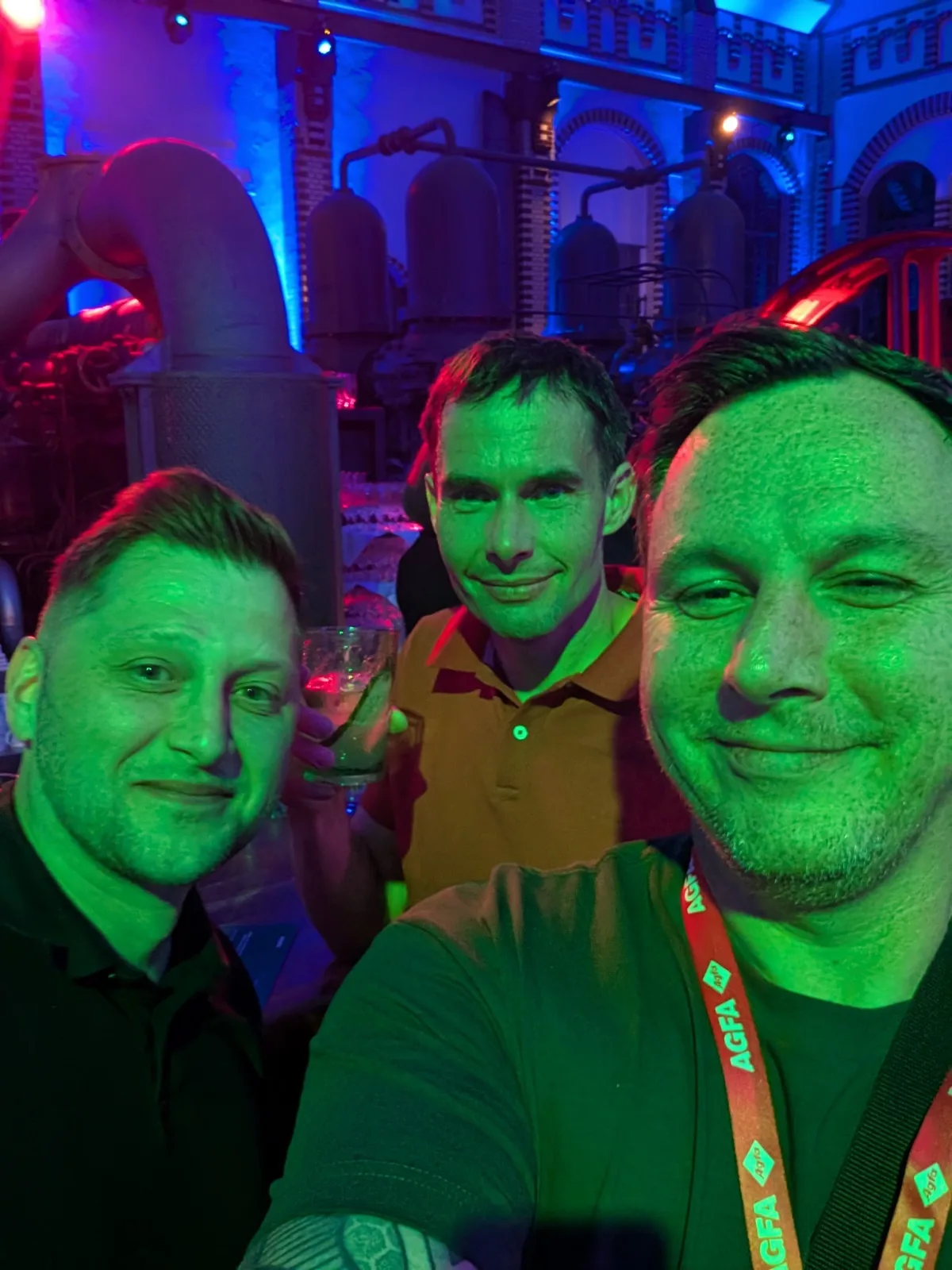 Selfie von drei Männern in grünem Licht, dahinter Industrieanlagen