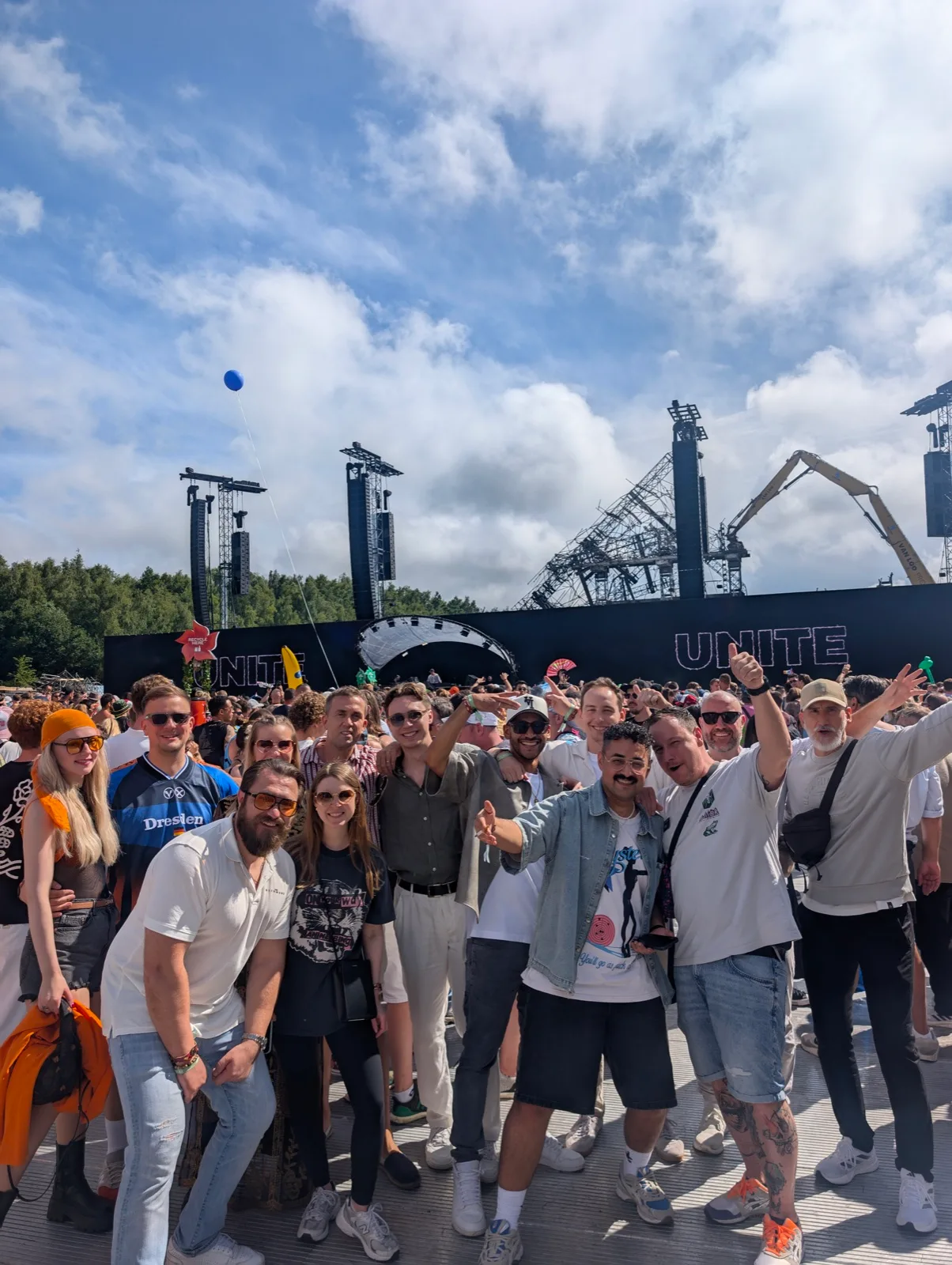 Gruppe vor einer Festivalbühne unter bewölktem Himmel