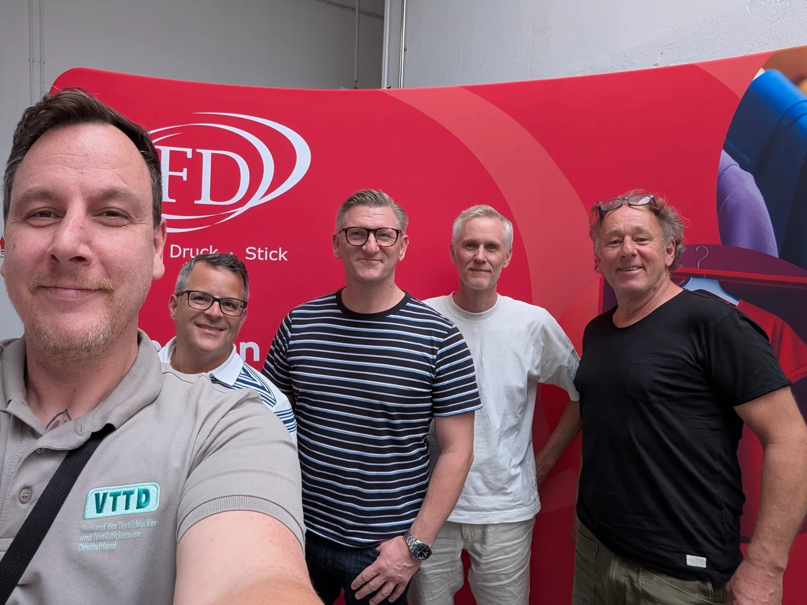 Selfie von fünf Männern vor der roten Wand eines Messestands