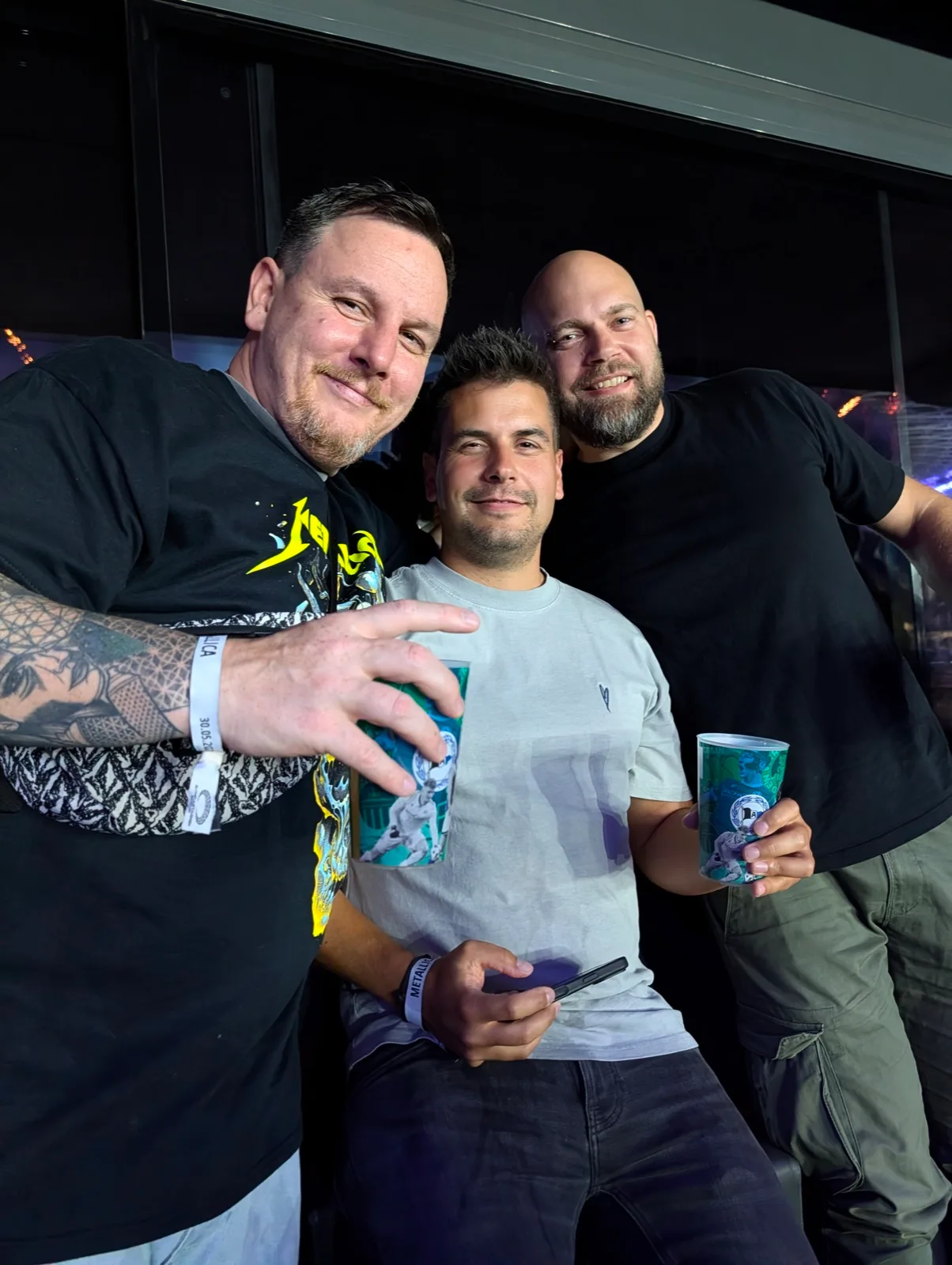 Drei Männer mit Bechern, Selfie in einem dunklen Innenraum