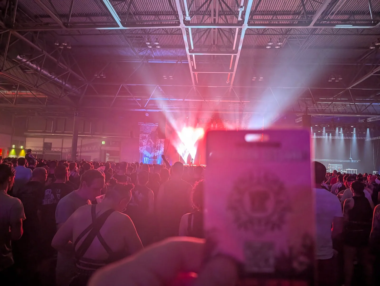 Konzertpublikum in einer Halle, ein Handy filmt die Bühne im Gegenlicht