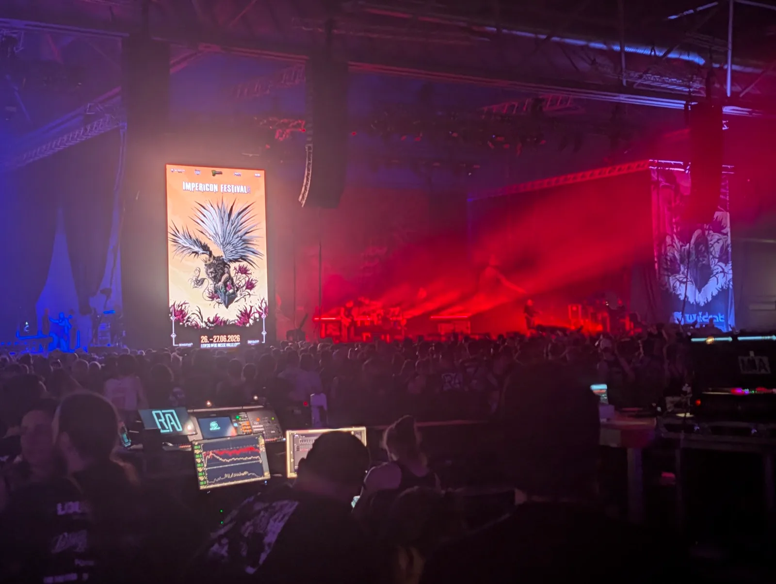 Festivalhalle mit rot-blauem Bühnenlicht, im Vordergrund das Mischpult