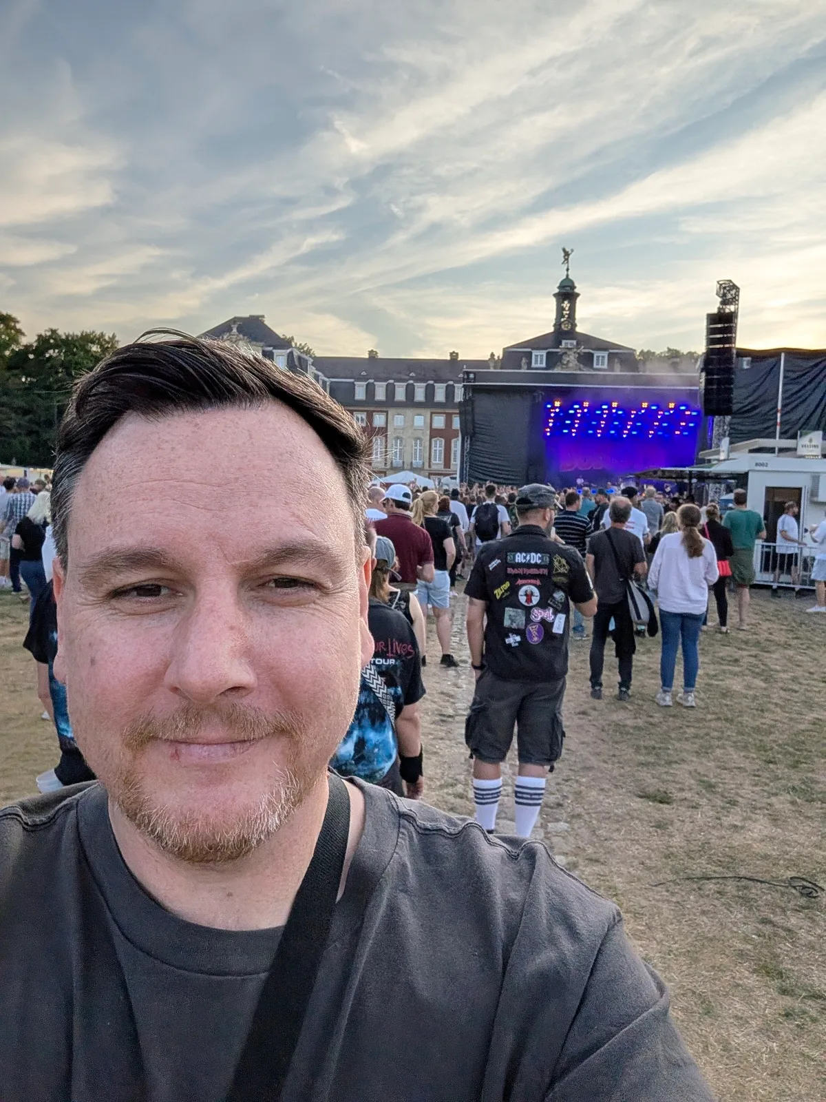 Selfie vor einer Open-Air-Bühne, dahinter Publikum und ein historisches Gebäude