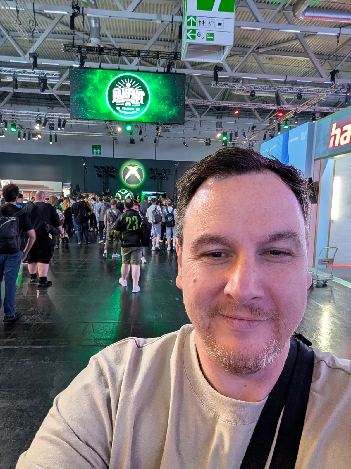 Selfie in einer Messehalle, im Hintergrund ein grün leuchtender Bildschirm und Besucher