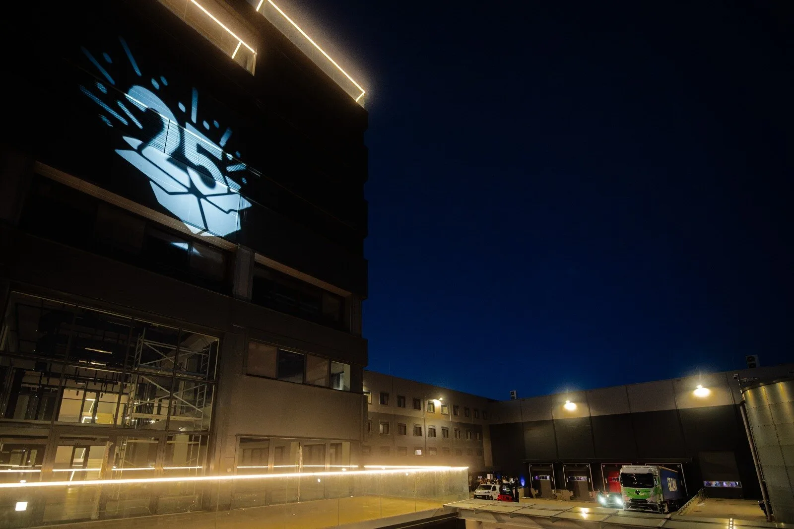 Building at night with the number 25 projected on the façade, lit loading bays in front