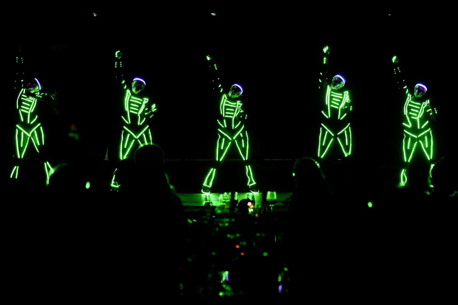 Five dancers in green glowing suits on a dark stage