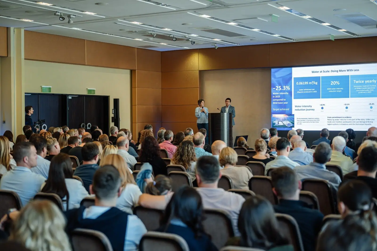 Lecture hall with an audience, two speakers at the lectern and a presentation on the screen
