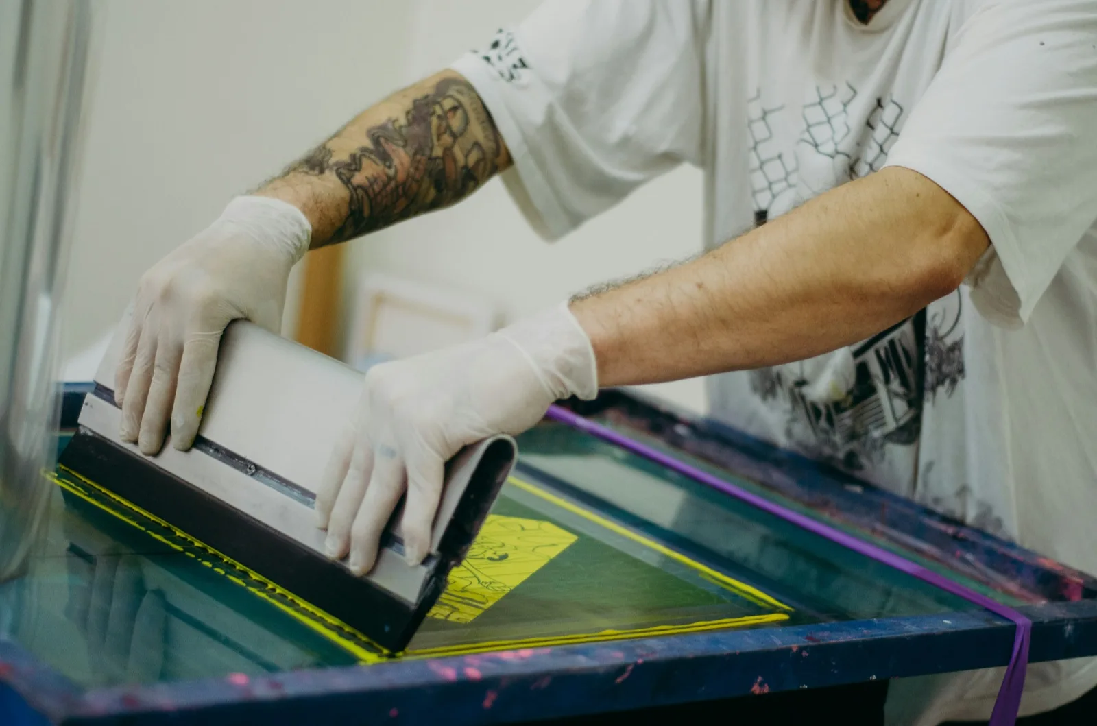 Siebdruck: Rakel zieht Farbe über das Sieb auf ein Shirt