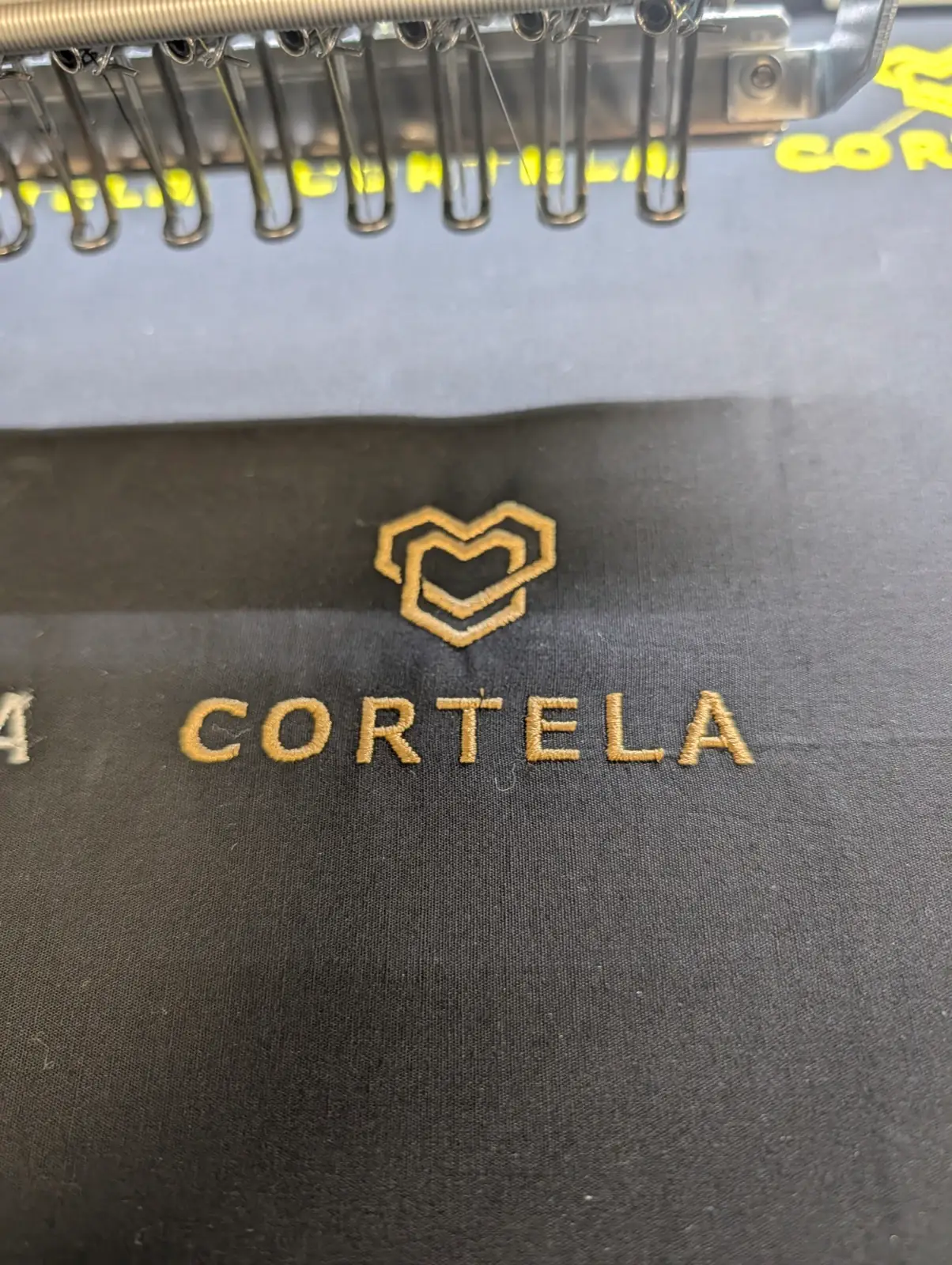 Logo CORTELA avec cœur brodé en or sur tissu sombre