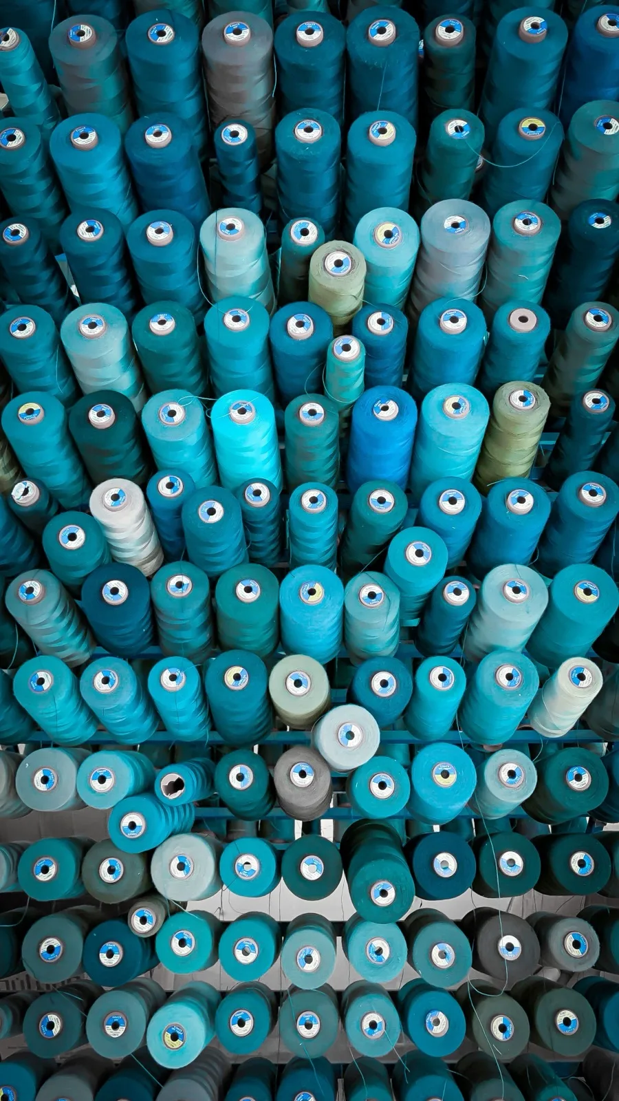 Regalwand mit hunderten Garnkonen in Blau- und Türkistönen