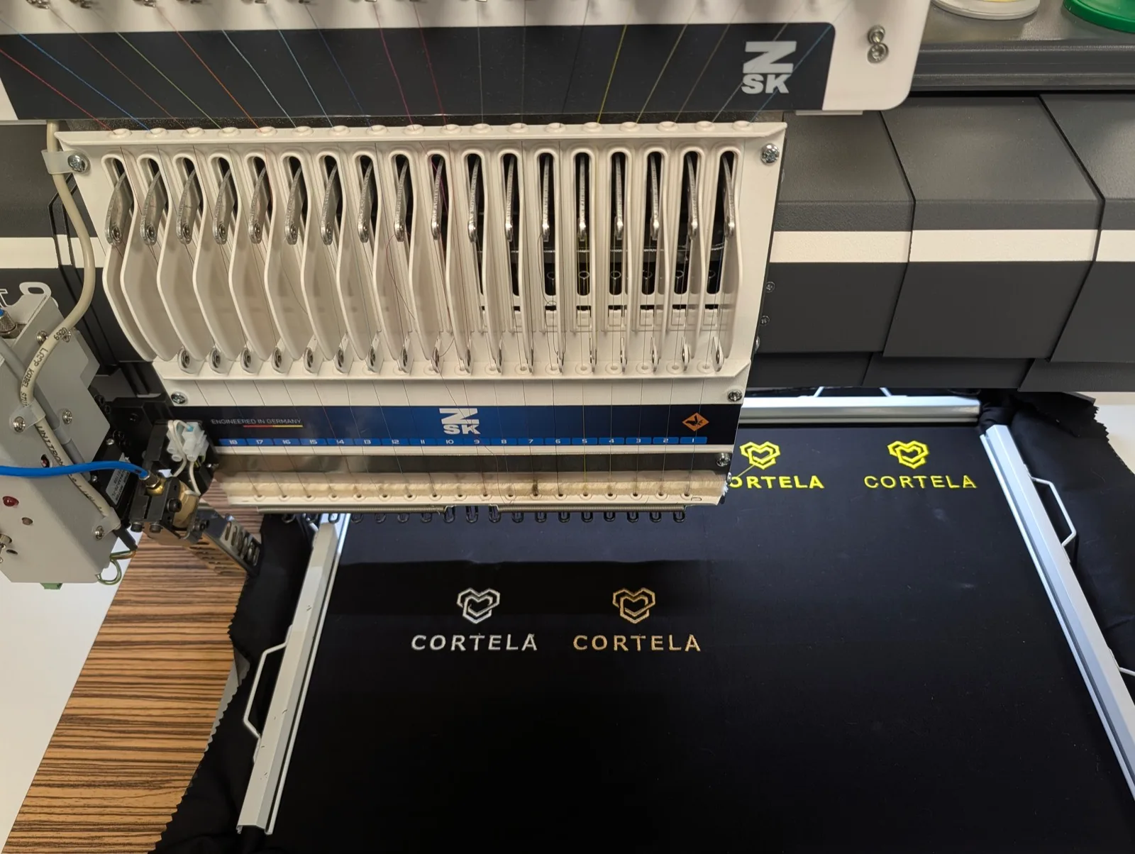 Rangée de logos CORTELA brodés sur tissu noir sous la tête de broderie