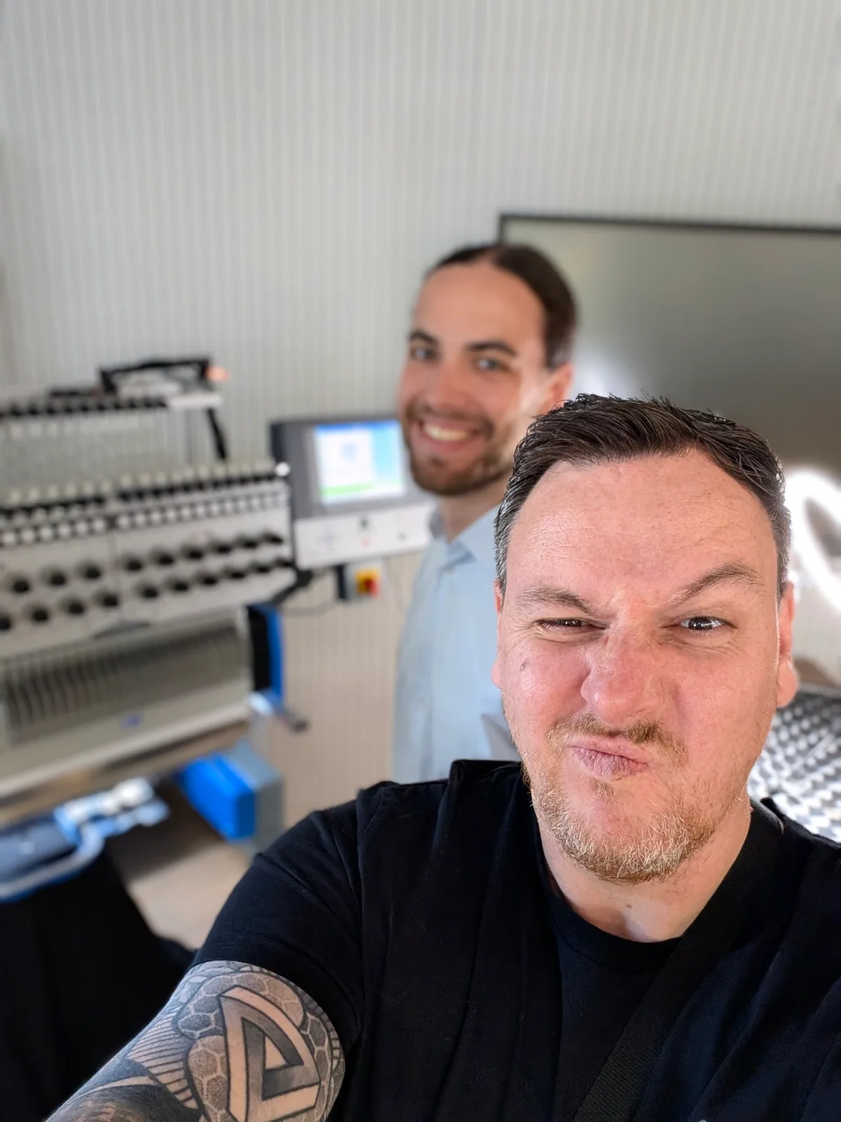 Selfie von zwei Männern vor einer Mehrkopf-Stickmaschine