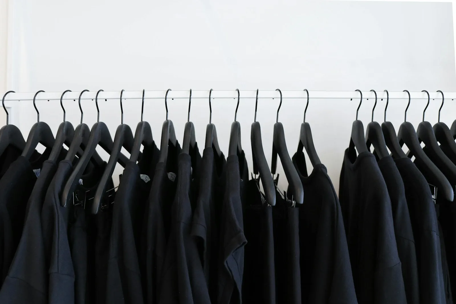 Kleiderstange mit schwarzen Shirts auf Bügeln